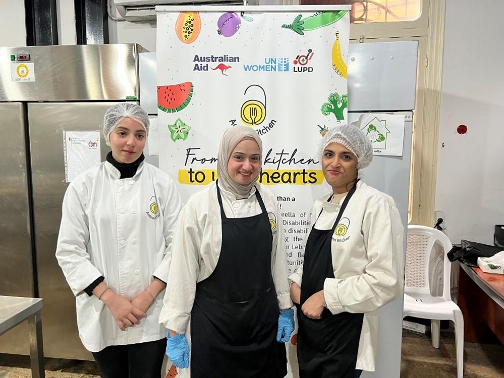 from left to right: Riwa, Hanan and Samira, posing in front of the Access Kitchen initiative’s roll-up.