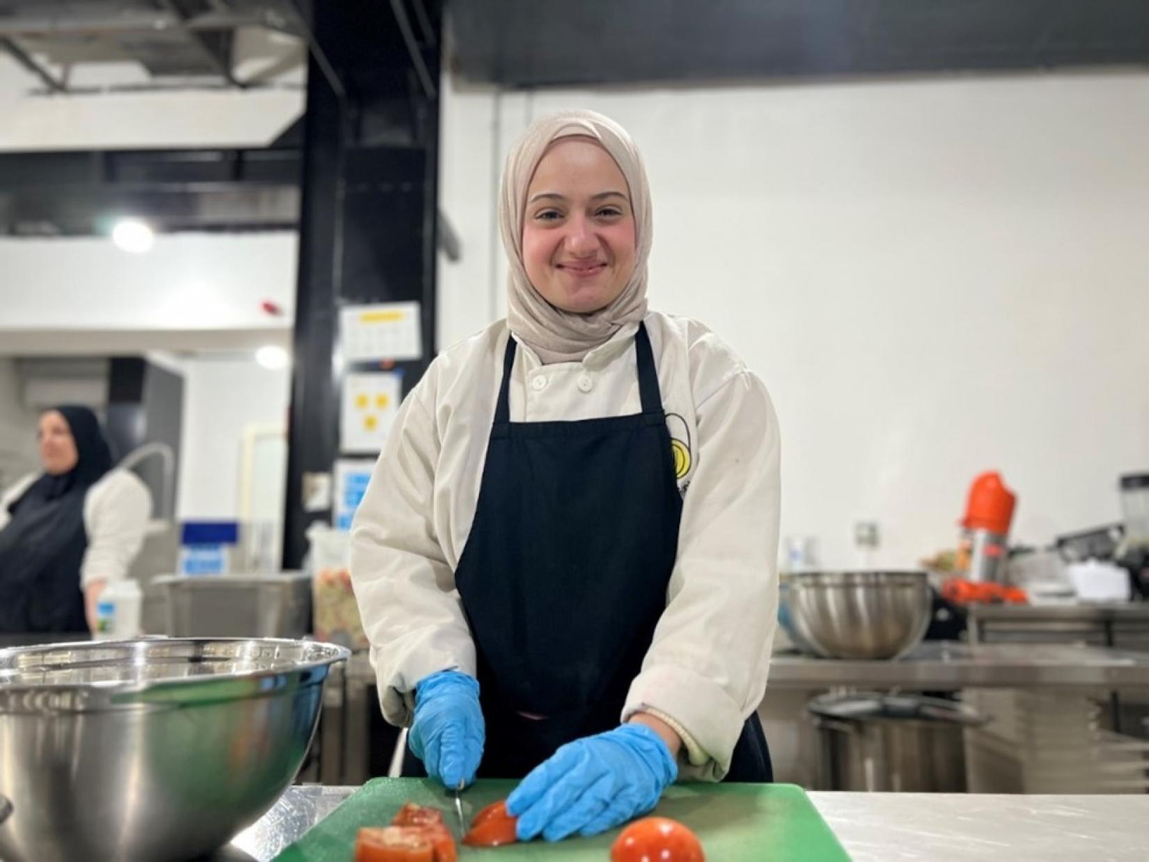 Hanan Bathatha, carefully chopping tomatoes for a delicious Lebanese Tabbouleh, destined to bring comfort and food to displaced families. 