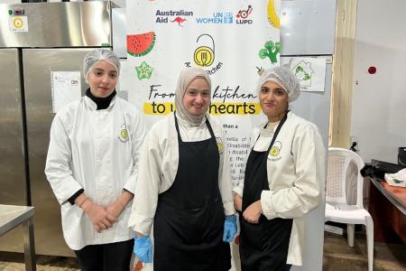 from left to right: Riwa, Hanan and Samira, posing in front of the Access Kitchen initiative’s roll-up.